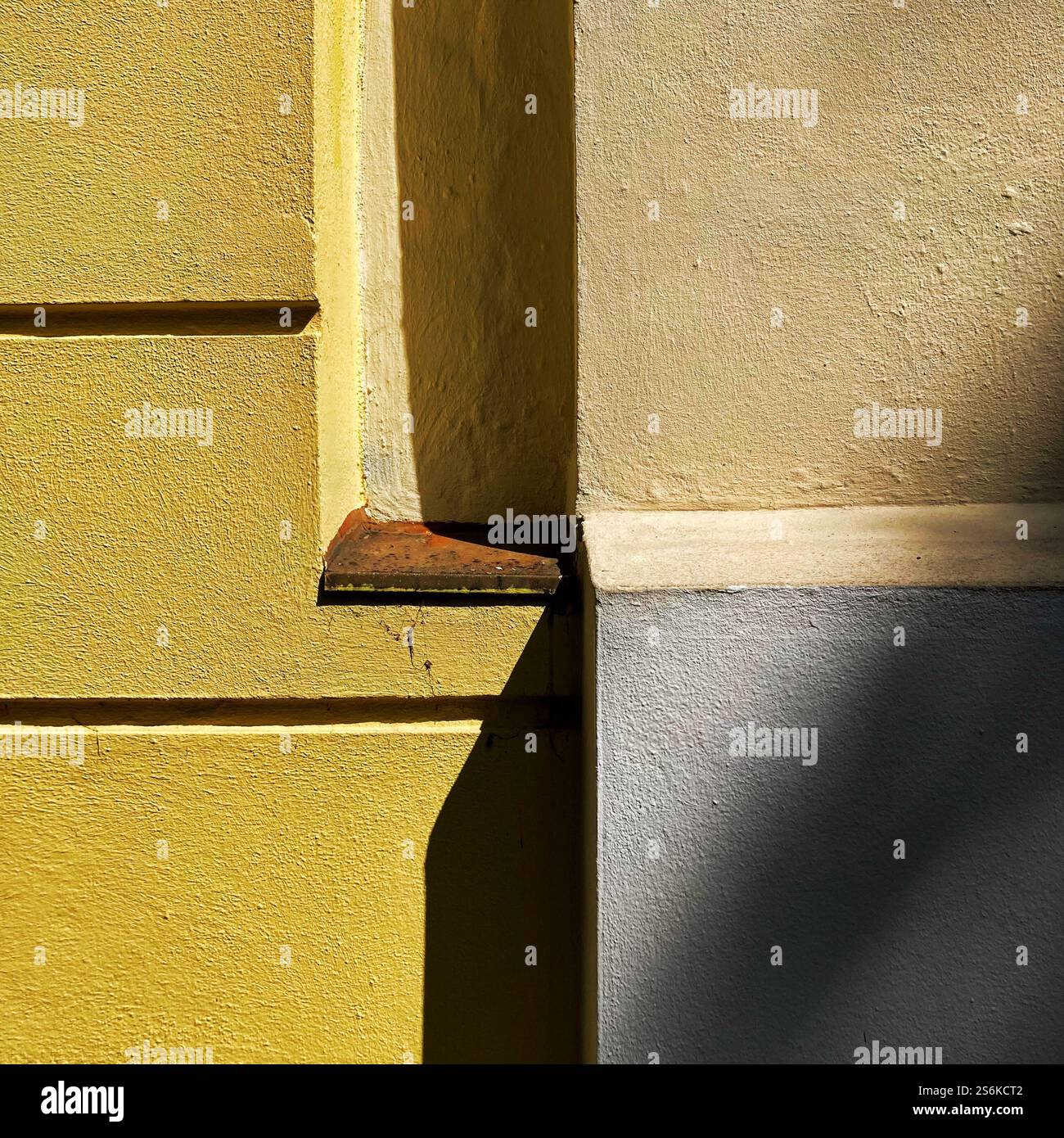 Geometrisches Muster, das durch Sonnenlicht und Schatten an einer Ecke aus gelben und beigefarbenen Wänden erzeugt wird. - Smartphone-aufgenommenes Stockfoto