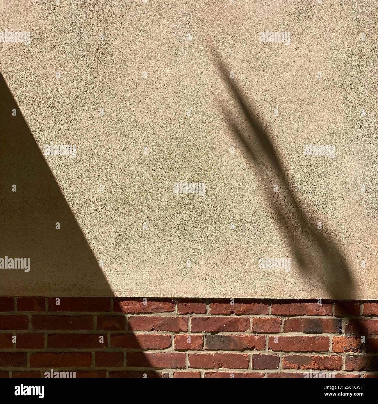 Schatten auf einer beigefarbenen Wand über einer Ziegelfassade mit minimalistischen architektonischen Texturen und natürlichem Licht - Smartphone-aufgenommenes Stockfoto