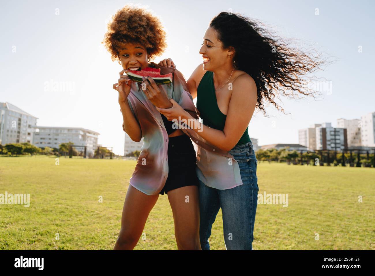 Zwei beste Freunde teilen sich einen lustigen Moment mit Wassermelone in einem sonnigen Park und fangen Freude, Freundschaft und den Geist des Sommers ein. Stockfoto