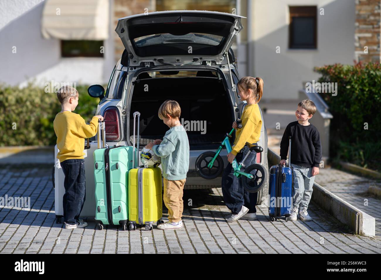 Kinder stehen neben einem Auto mit großen Koffern am Kofferraum, bereit für eine Reise. Stockfoto