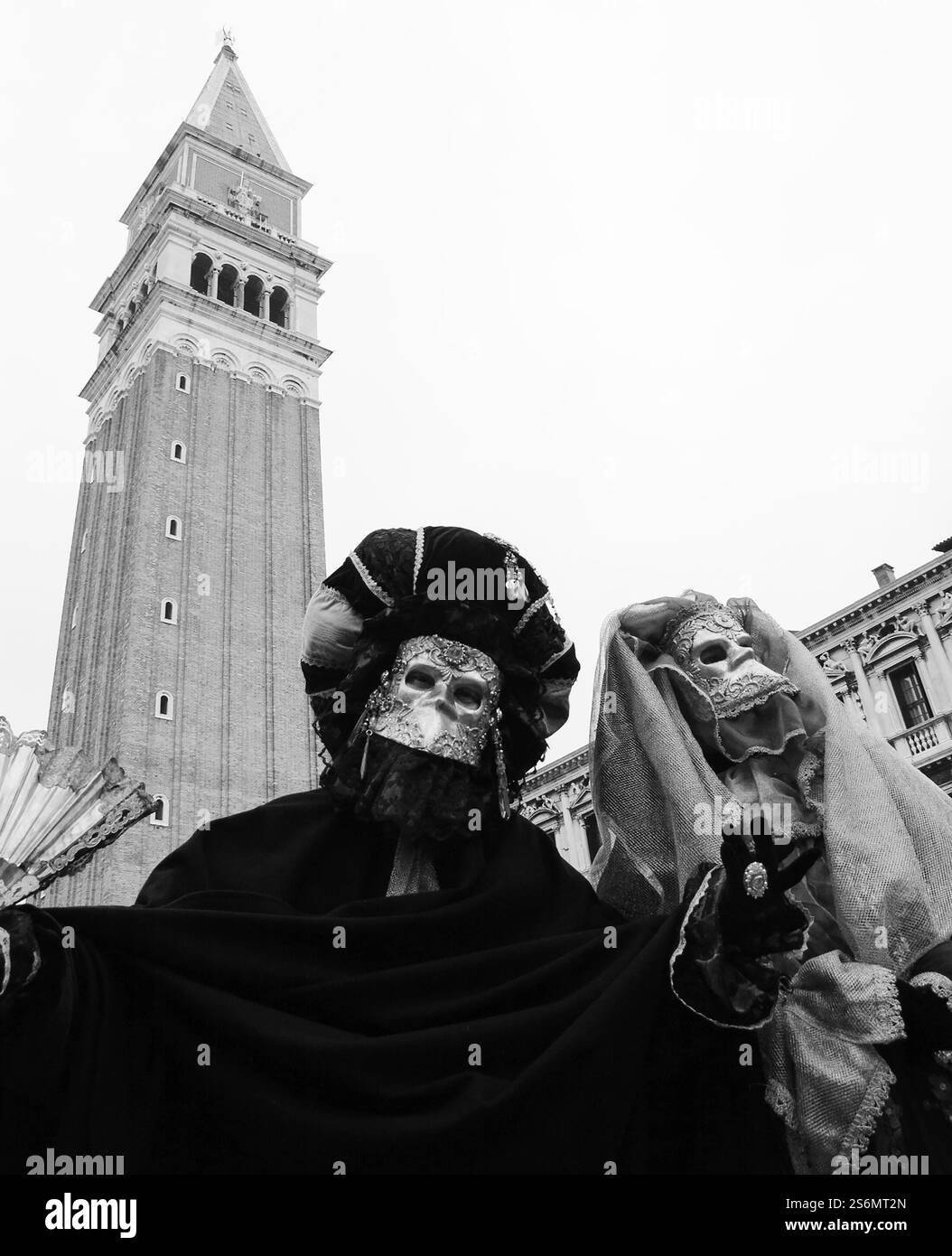 Zwei gruselige Masken auf dem Markusplatz während des traditionellen Karnevals mit Campanile-Glockenturm im Hintergrund. Venedig, Italien. Schwarzweißfoto Stockfoto