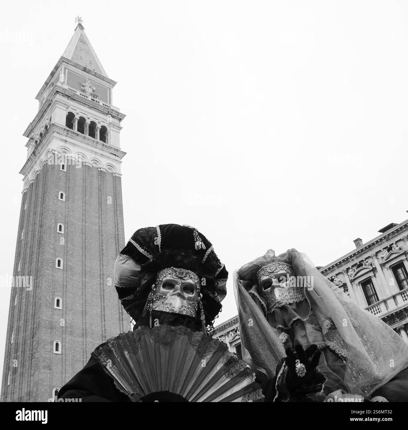Zwei gruselige Masken auf dem Markusplatz während des traditionellen Karnevals mit Campanile-Glockenturm im Hintergrund. Venedig, Italien. Schwarzweißfoto Stockfoto