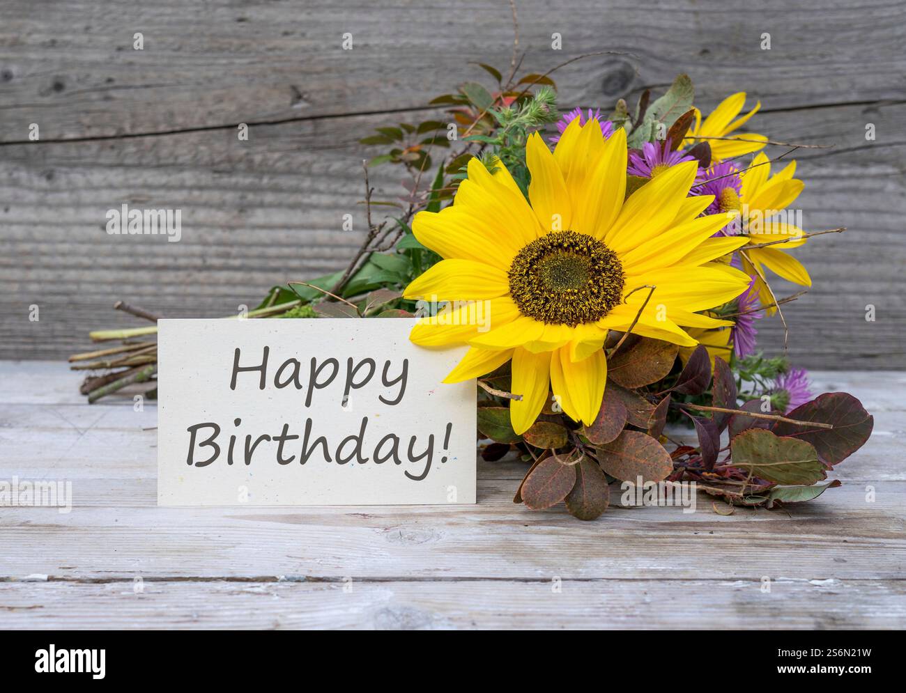 Geburtstagskarte mit dem englischen Text: Happy Birthday liegt vor einem herbstlichen Blumenstrauß mit Sonnenblume Stockfotografie
