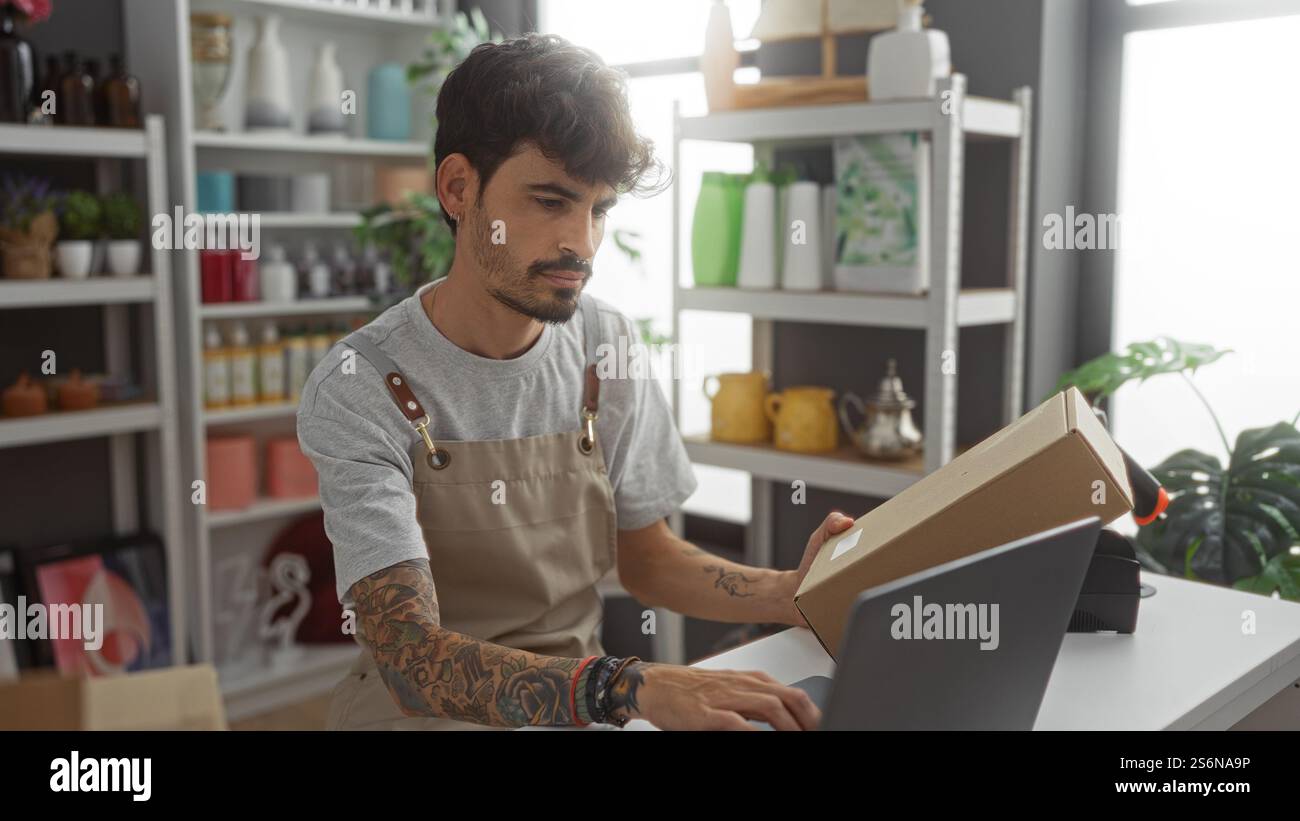 Mann arbeitet mit Laptop und Paket in einem Wohnkultur-Geschäft mit Regalen von bunten Gegenständen im Hintergrund Stockfoto