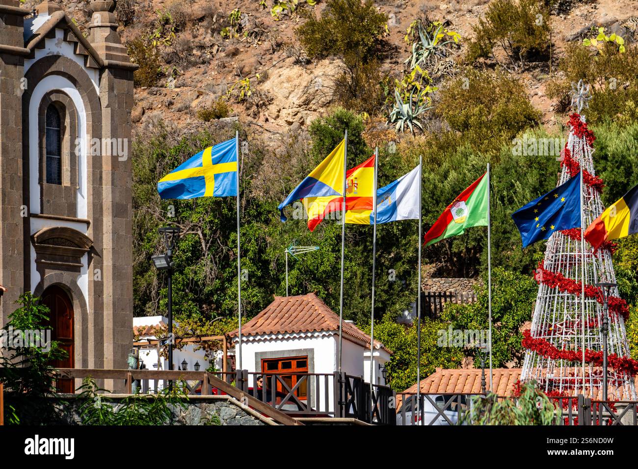 Eine Gruppe von Fahnen hängt an einem Baum vor einer Kirche. Die Flags haben unterschiedliche Farben und Größen und sind so angeordnet, dass sie erzeugen Stockfoto