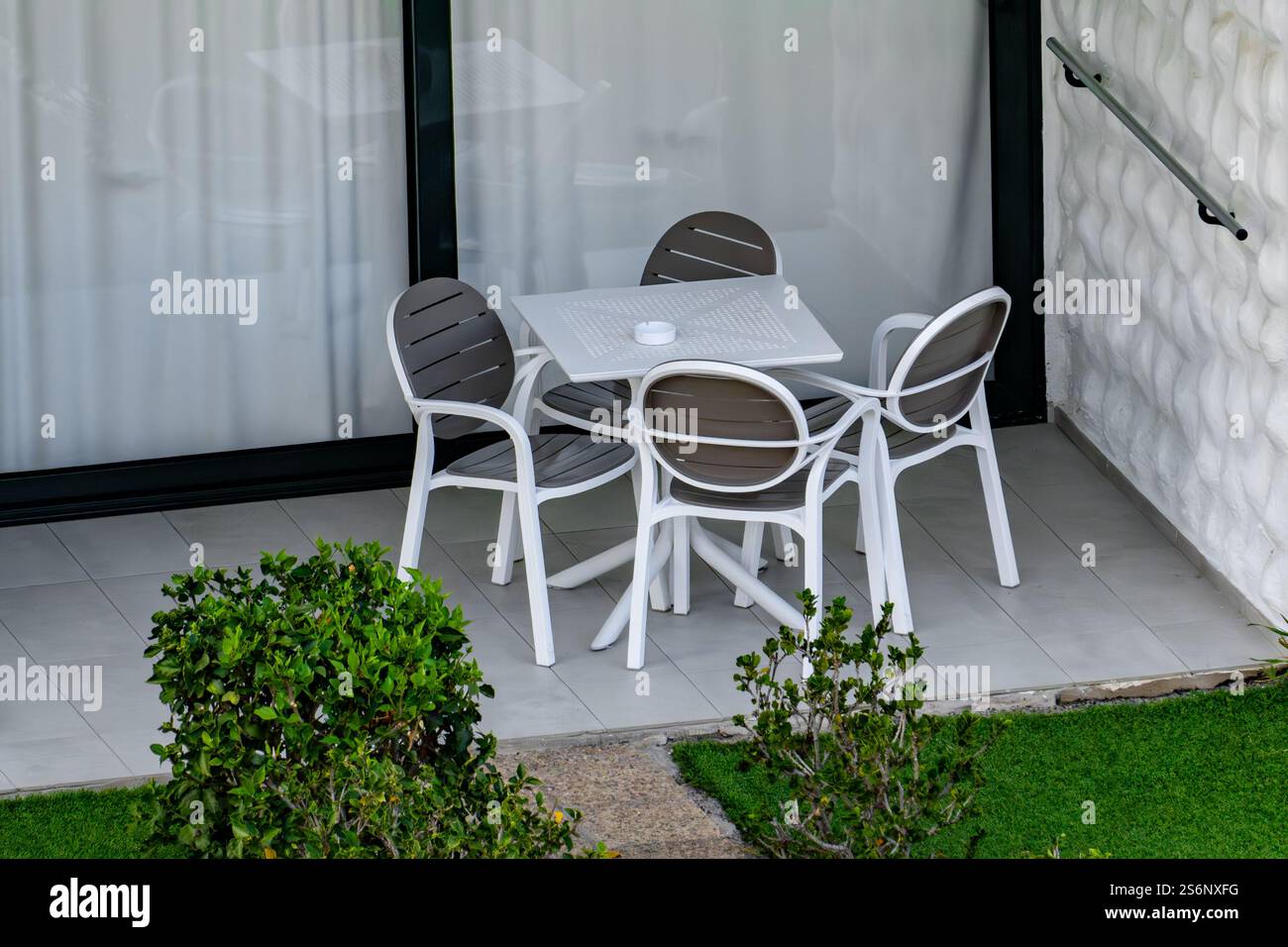 Eine weiße und graue Terrasse mit vier Stühlen und einem Tisch. Die Stühle sind um den Tisch herum angeordnet, und in der Nähe befindet sich eine Topfpflanze. Rela-Konzept Stockfoto