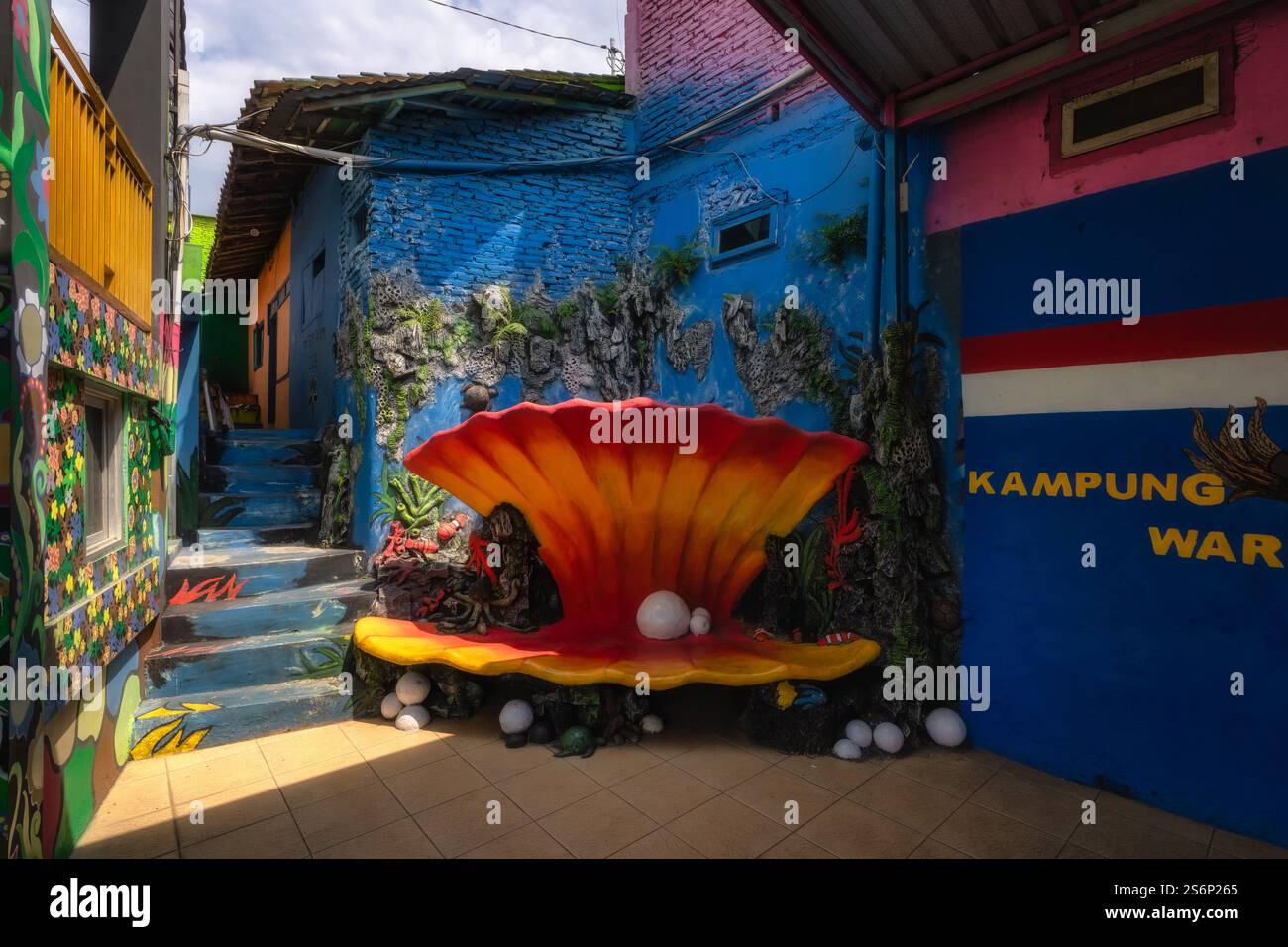 Malang, Java, Indonesien, 2. Oktober 2024 Erkunden Sie eine lebhafte Gasse mit einem komplizierten Wandgemälde und einer fesselnden Muschelskulptur, die die lokalen Kommuniquen zeigt Stockfoto