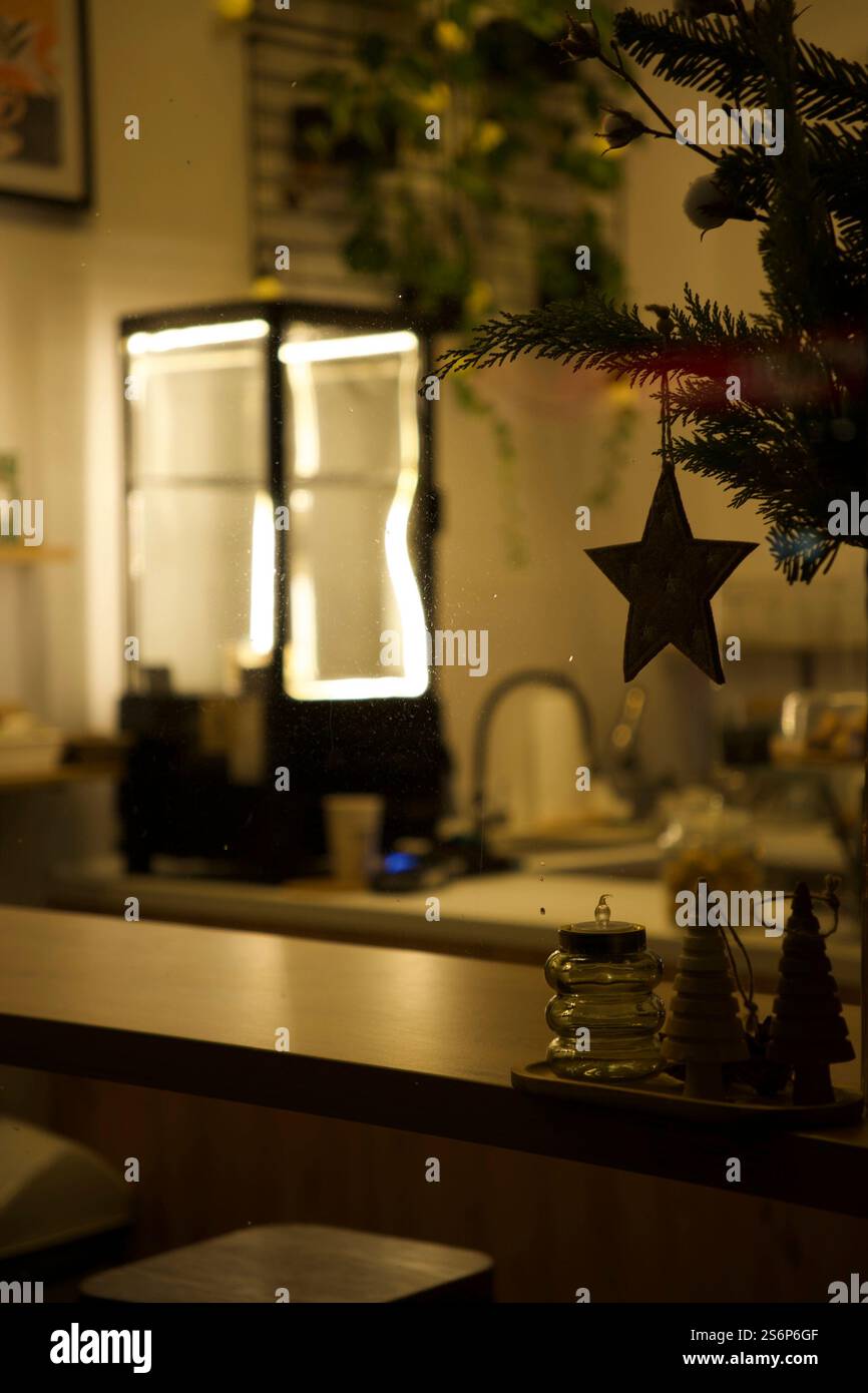 Ein Weihnachtsbaum mit einem hölzernen Sternenschmuck setzt den Fokus, eingerahmt vom sanften Leuchten eines verschwommenen Dessertkühlschranks Stockfoto