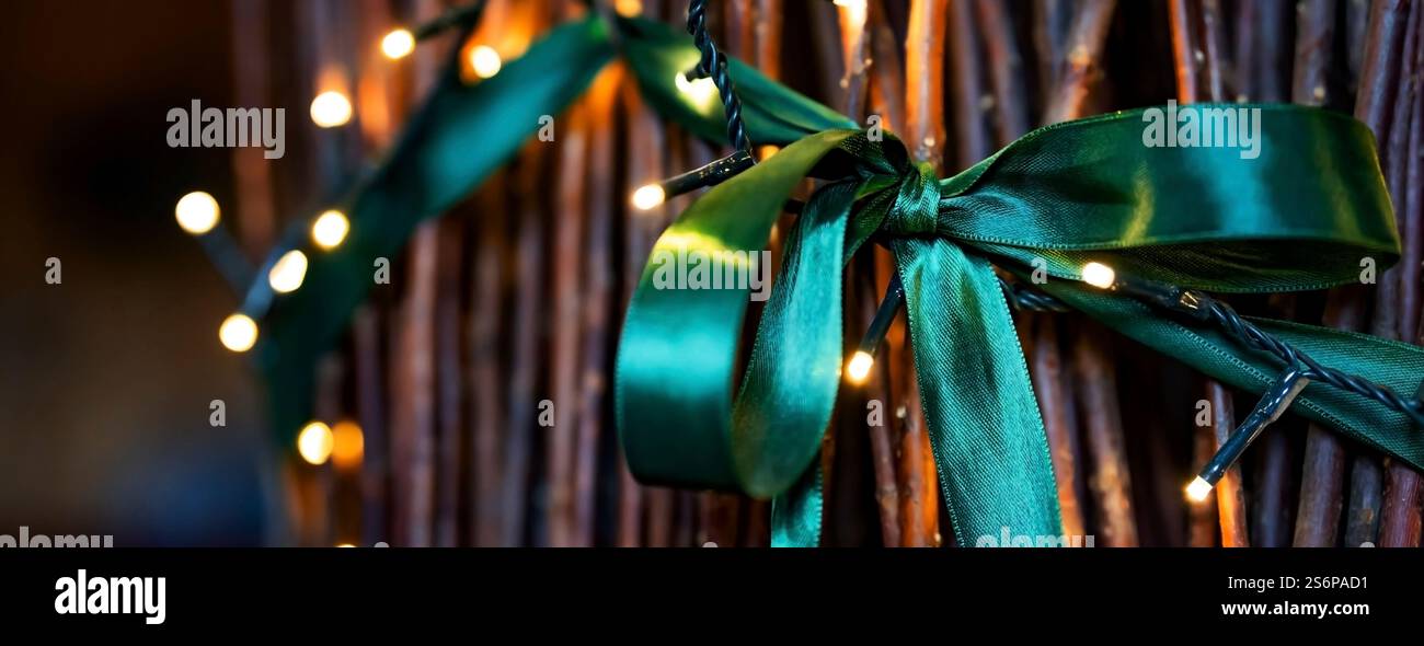 Festliche, glänzende grüne Schleife mit Bokeh-Lichtern an einem weihnachtsbaum aus Weidenzweigen. Horizontaler Hintergrund mit Urlaubsstimmung und kurzer Schärfentiefe. Stockfoto