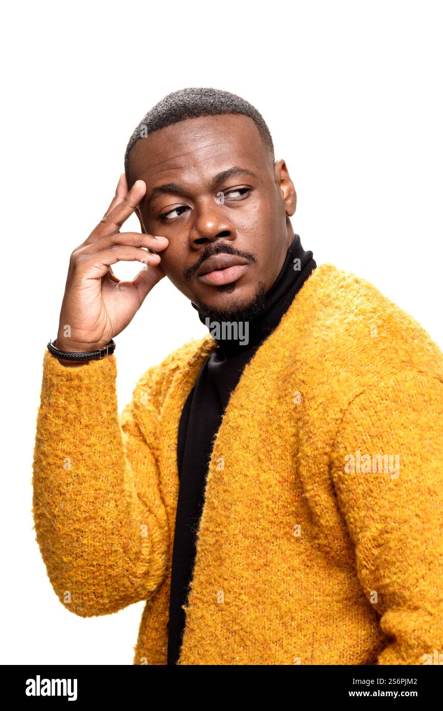 Ein nachdenklicher Mann in einem Senfpullover und schwarzem Rollkragen posiert mit kontemplativem Ausdruck und Handgeste vor neutralem Hintergrund, Showcasi Stockfoto