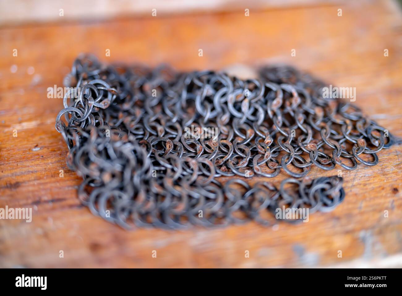 Eine Kette von Metallgliedern liegt auf einer Holzoberfläche. Die Kette ist alt und verrostet, und sie ist ein Schmuckstück. Die Szene ist etwas melancholisch Stockfoto