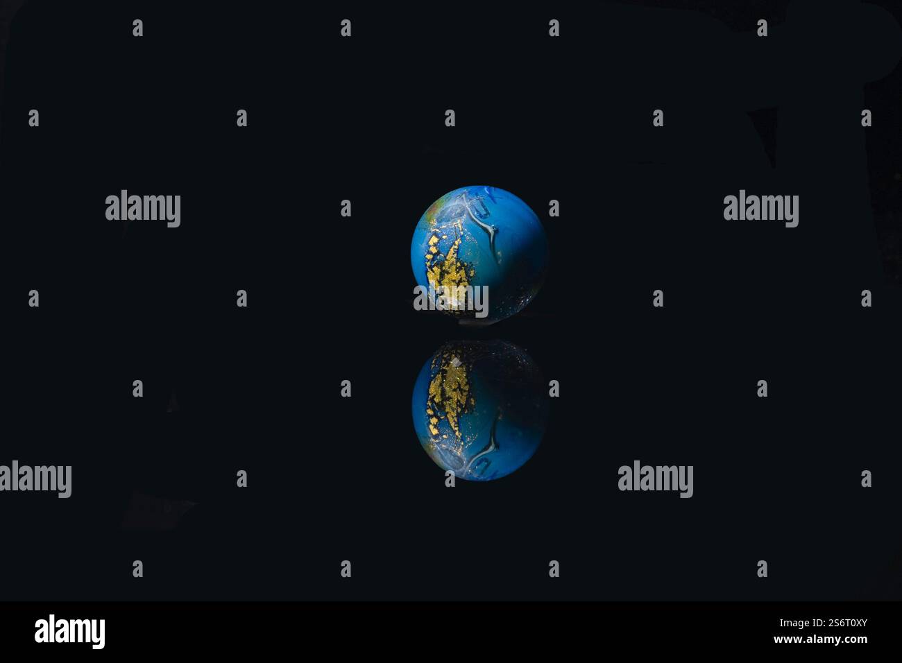 Glänzende blaue und goldene Kugel mit kompliziertem Design auf reflektierender Oberfläche Stockfoto