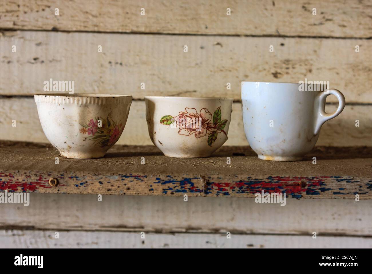 Drei weiße Tassen mit Blumenmotiven sitzen auf einem Regal. Die Becher sind schmutzig und scheinen alt zu sein Stockfoto