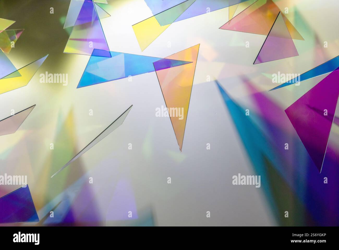 Abstraktes Hintergrundfoto mit bunten transparenten Kunststoffdreiecken, die helle Schatten auf die weiße Wand werfen Stockfoto