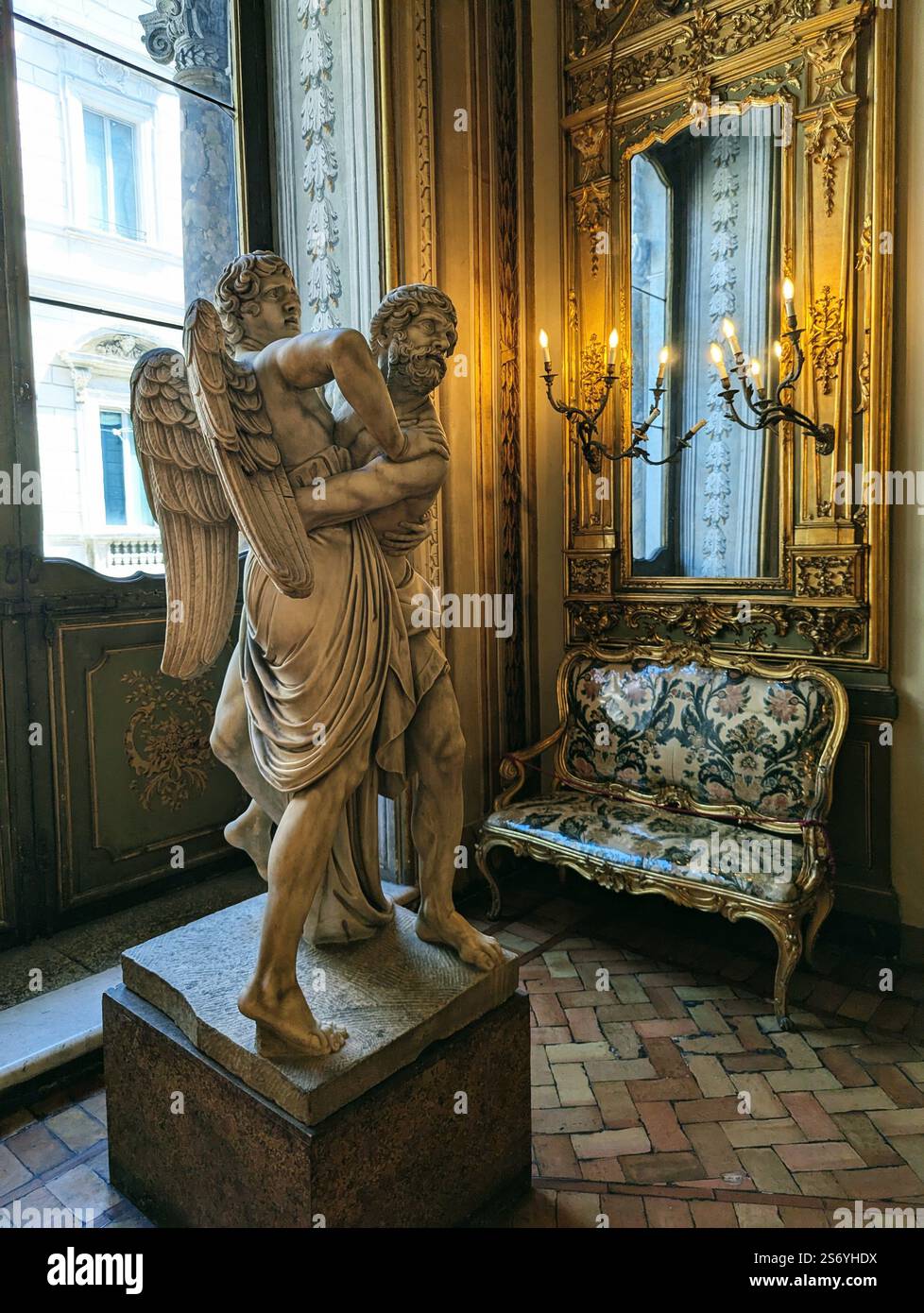 Eine Marmorstatue eines Engels, der einen bärtigen Mann trägt, steht in einem reich verzierten Raum mit einem vergoldeten Spiegel, antiken Wandlampen und einer luxuriösen Bank Stockfoto