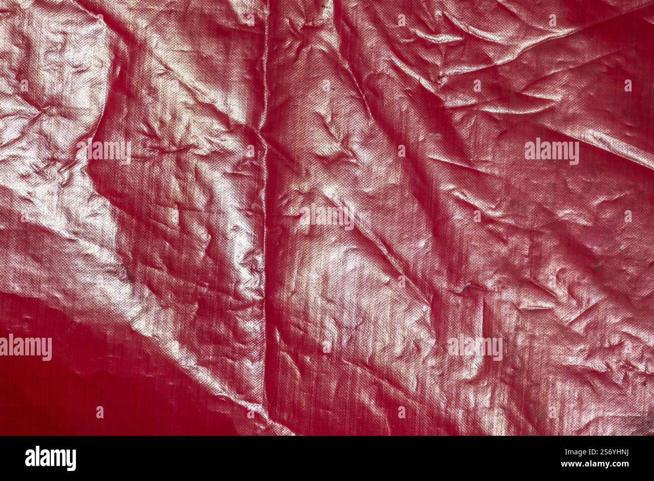 Glänzendes rotes Frontlicht eines alten, verkrusteten Banners, abstraktes Hintergrundfoto. Frontlit-Bannergewebe laminiert, aus Polyester-Mesh mit einem speziellen Doppel Stockfoto