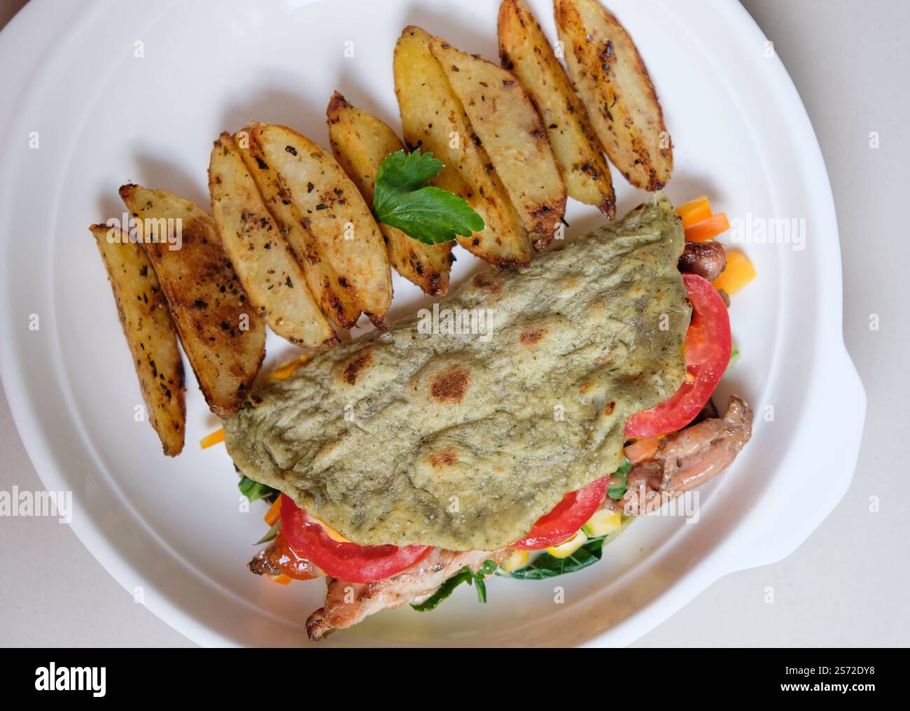 Gebackene Kartoffelscheiben und Tortilla-Wrap mit gebratenem Huhn und Vegeteble, serviert auf einem Teller. Stockfoto