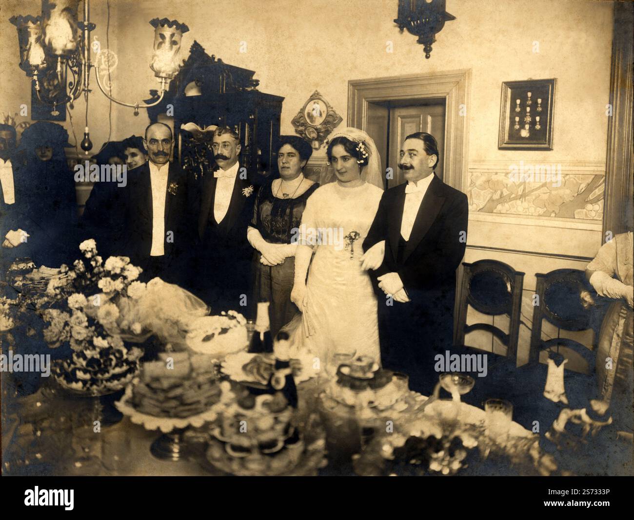 1900 n. Chr., ITALIEN : der Hochzeitstag ( möglich in Ligurien oder in der Nähe von Genova). Mittagessen im Elternhaus der Braut, posiert das Brautpaar mit seinen Eltern vor dem gedeckten Tisch und der Hochzeitstorte. Unbekannter Fotograf. - NOZZE - abito bianco da SPOSA - SPOSI - SPOSO - Handschuhe - guanti - MARITO E MOGLIE - HOCHZEIT Brautkleid PARTY - BRAUT - Cerimonia - XX JAHRHUNDERT - NOVECENTO - 1900er Jahre - TORTA NUZIALE - tavola imbandita - PRANZO - Thulle - Tüll - Velo - Schleier - weißes Kleid - abito vestito bianco da cerimonia - 900 900 - PAAR Stockfoto