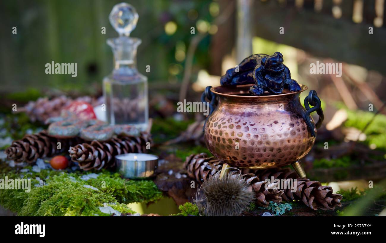 Ein Kupferkessel, Glasflasche, Tannenzapfen, Tonfrösche auf moosigem Hintergrund. Stockfoto