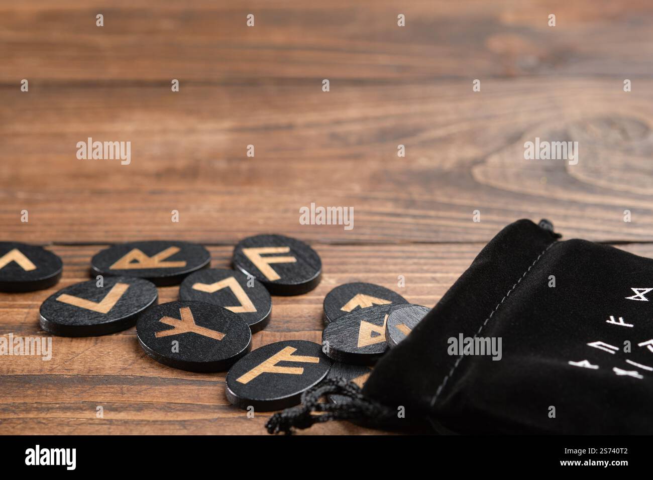Eine hölzerne Rune für Weissagung, Magie und spirituelle Praktiken, ausgestellt mit einem schwarzen Samtbeutel und leeren Platz auf einem Holztisch. Stockfoto
