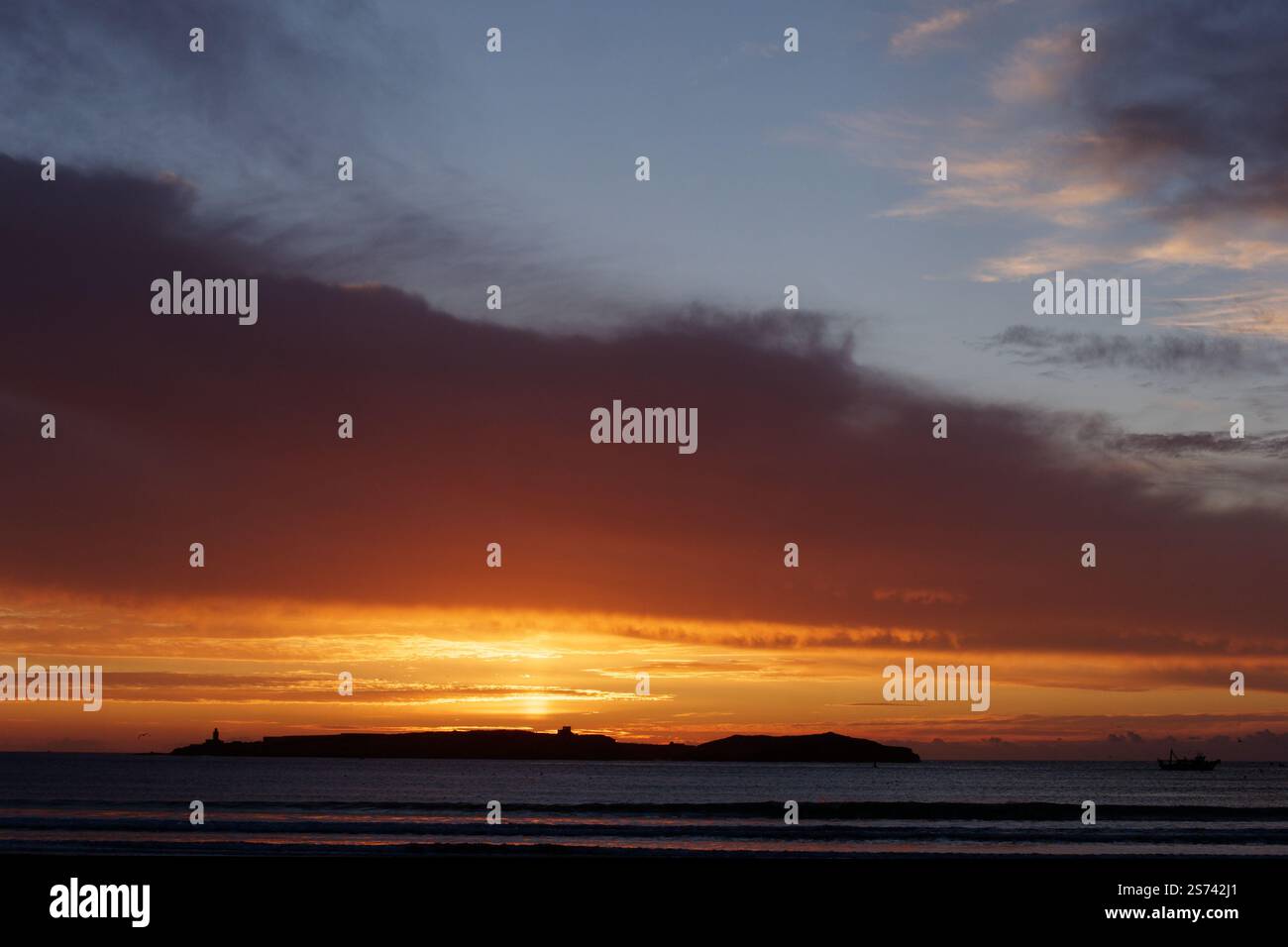Dramatische dunkle Wolken bei Sonnenuntergang mit blauem Himmel über einer Insel vor der Küste von Essaouira, Marokko. Januar 2025 Stockfoto