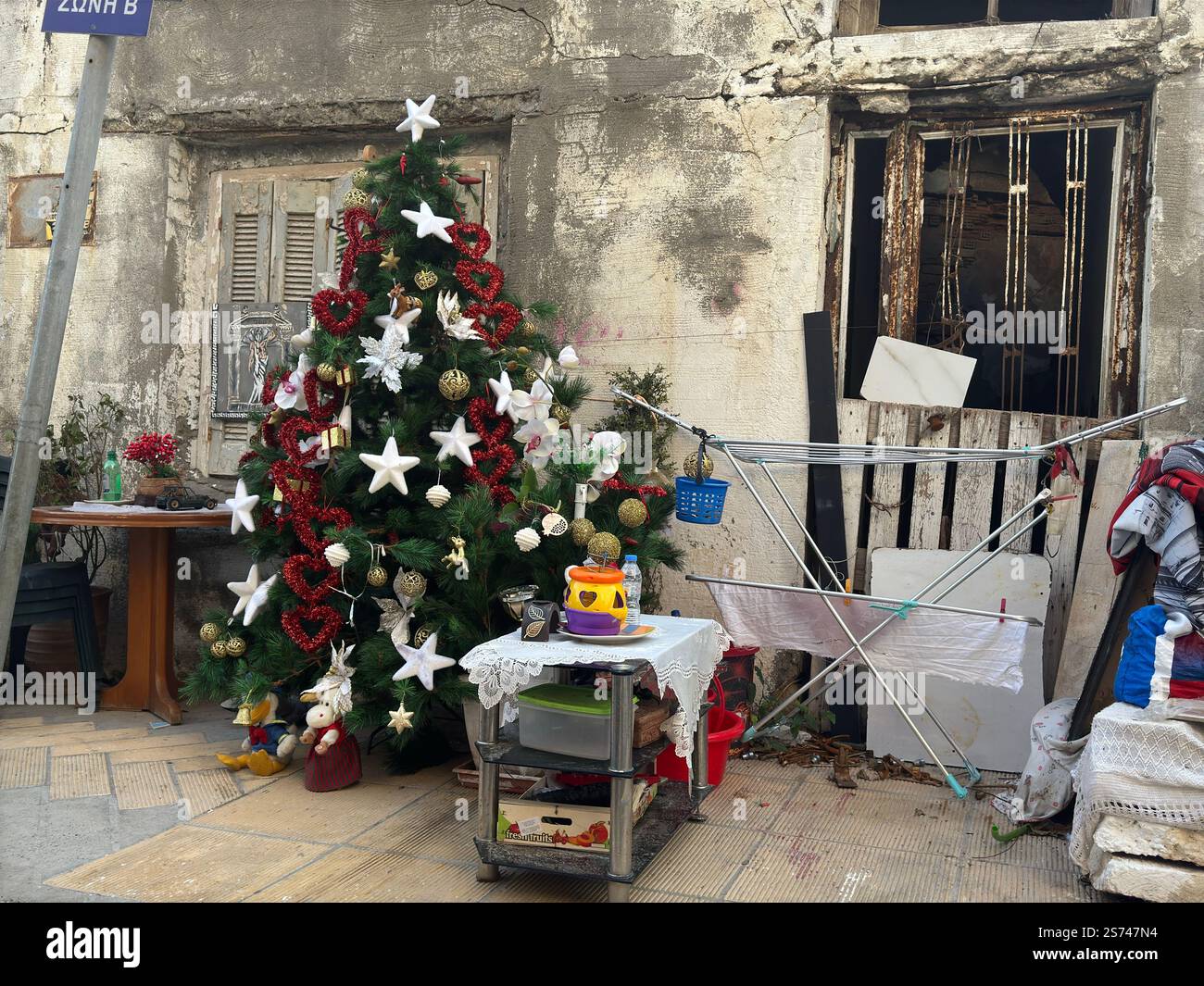 Ein wunderschön geschmückter Weihnachtsbaum vor einem armen oder verlassenen Haus. Weihnachtsstimmung in der Nachbarschaft. Blick von der Straße Stockfoto