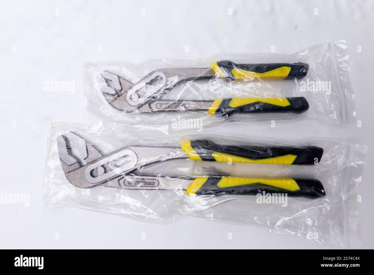 Zwei brandneue Zangen mit Feder und Nut mit gelben und schwarzen Griffen sind in Kunststoff gewickelt und auf weißem Hintergrund ausgelegt Stockfoto