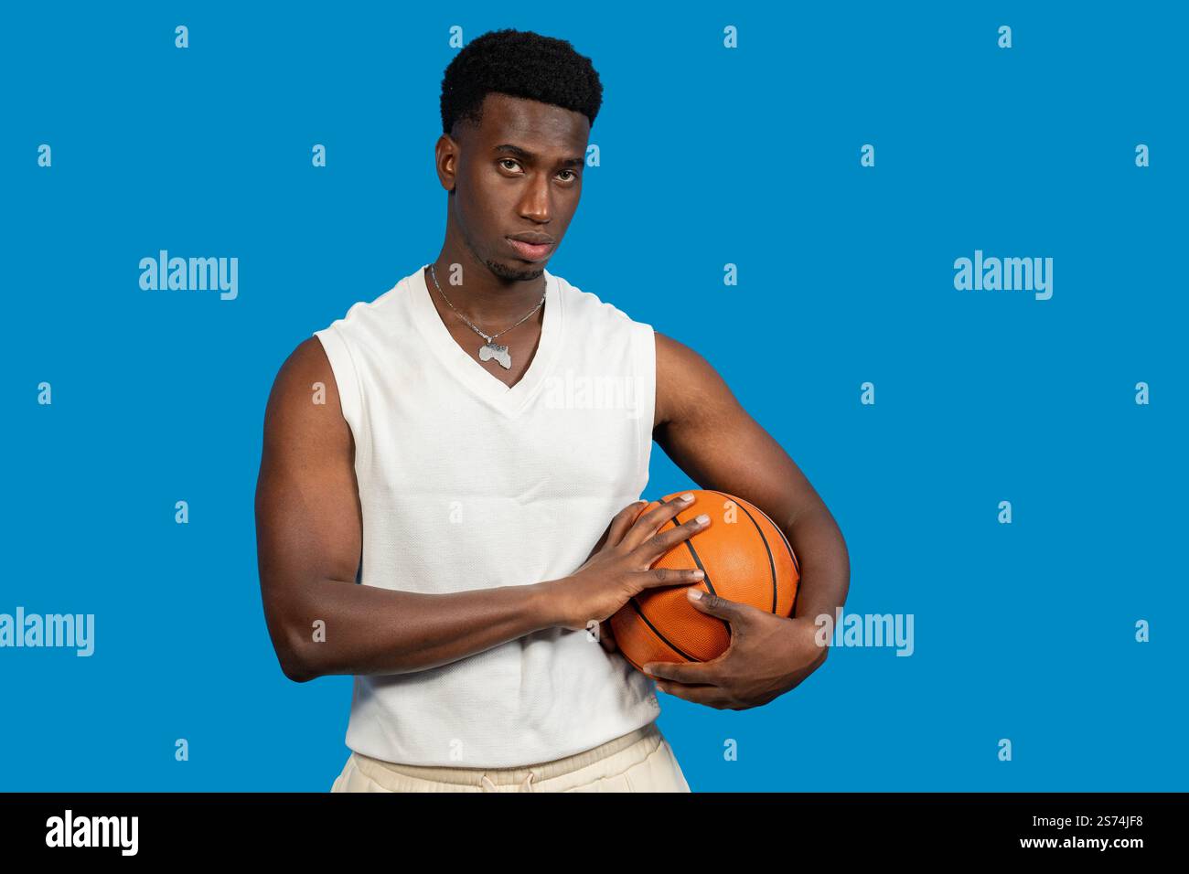 Junger afroamerikanischer Basketballspieler, der Ball hält und auf blauem Hintergrund selbstbewusst aussieht Stockfoto