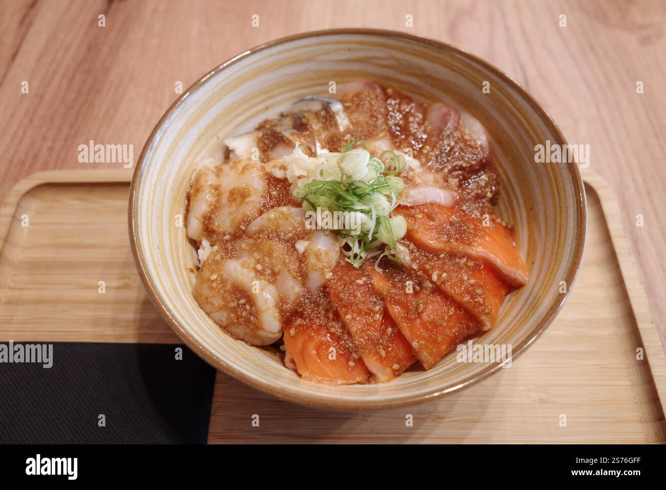 Ein wunderschön präsentierter japanischer Donburi mit frischem rohem Lachs und Jakobsmuscheln, serviert über Reis in einer Keramikschale mit Spiralmuster. Stockfoto