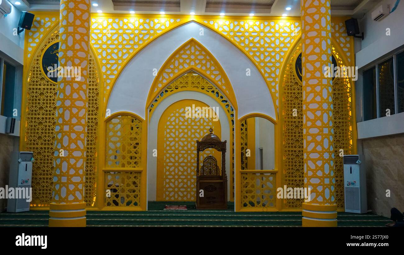 Das wunderschön gestaltete Innere einer Moschee mit komplexen gelben Gitterarbeiten, bogenförmigen Türöffnungen und dekorativen Säulen. Der Raum ist gut beleuchtet und Stockfoto