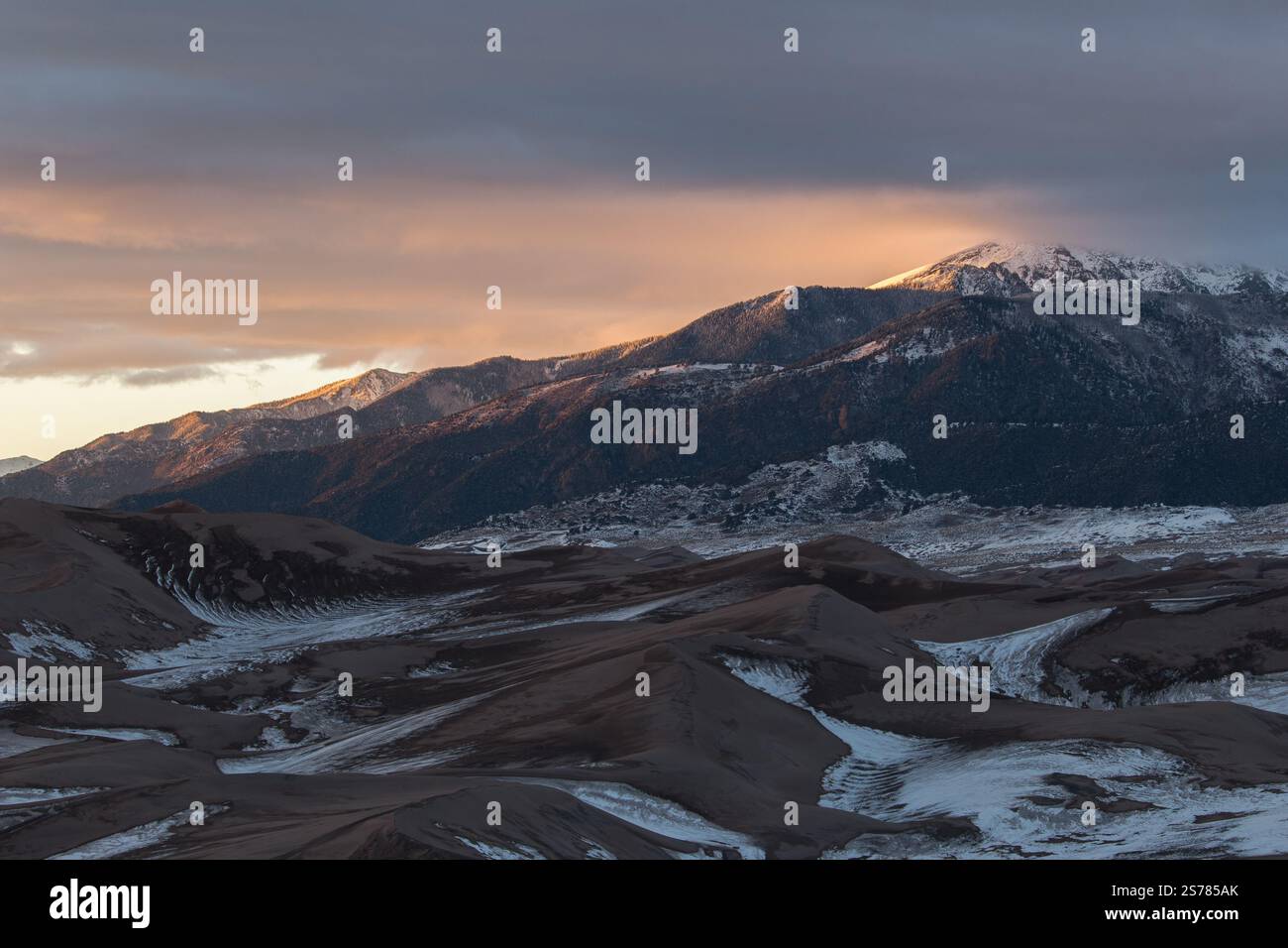 Great Sand Dunes National Park, Colorado, bei Sonnenuntergang mit schneebedeckten Dünen im Schatten und sonnendurchfluteten Berggipfeln. Eine malerische Winterlandschaft. Stockfoto