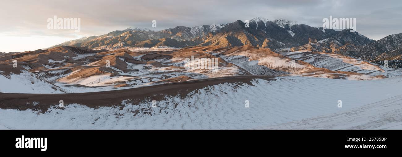 Ein Panoramablick auf den Great Sand Dunes National Park, Colorado, bei Sonnenuntergang. Schneebedeckte Dünen stehen im Kontrast zu einem lebendigen Himmel und fernen Bergen. Stockfoto
