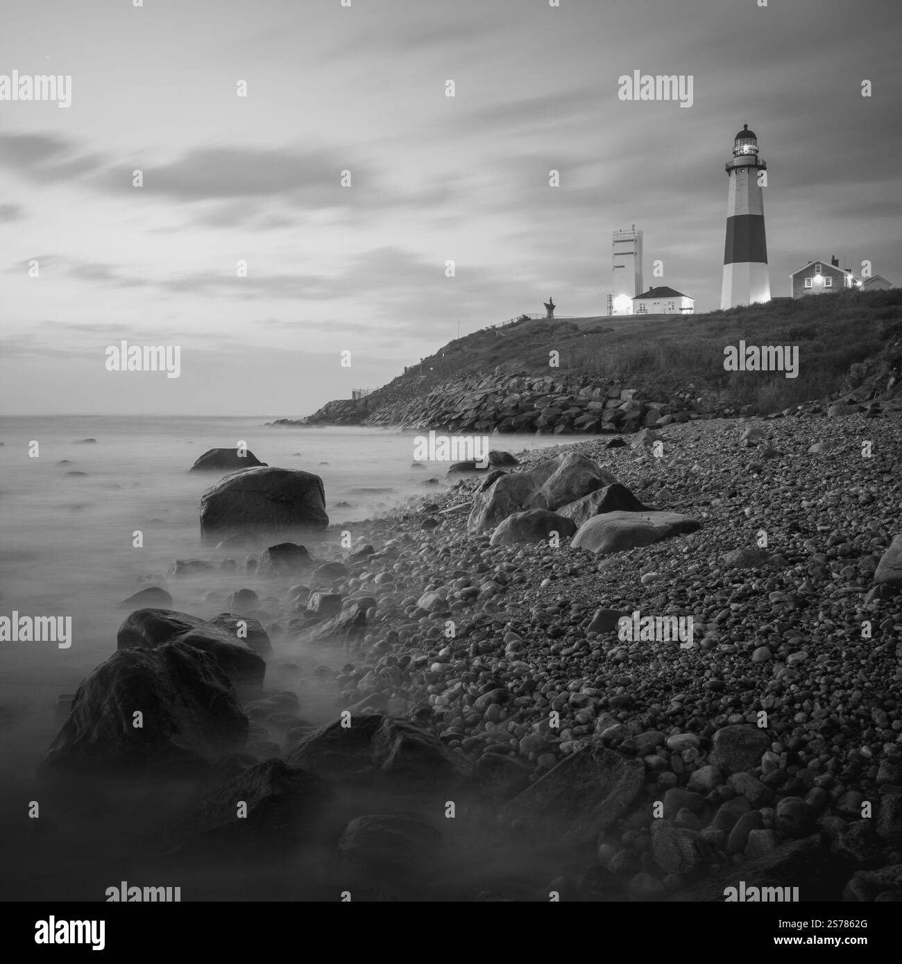 Eine lange Schwarzweißbelichtung des Montauk Lighthouse in New York mit zerklüfteten Felsen und einer ruhigen Meereslandschaft. Stockfoto