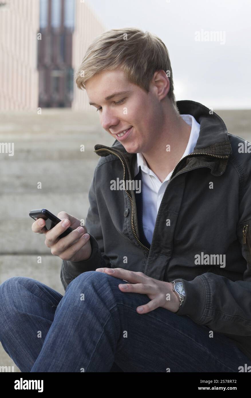 Junger blonder, gutaussehender, lächelnder Mann, der auf seinem Handy schreibt, Belgien, Europa Stockfoto