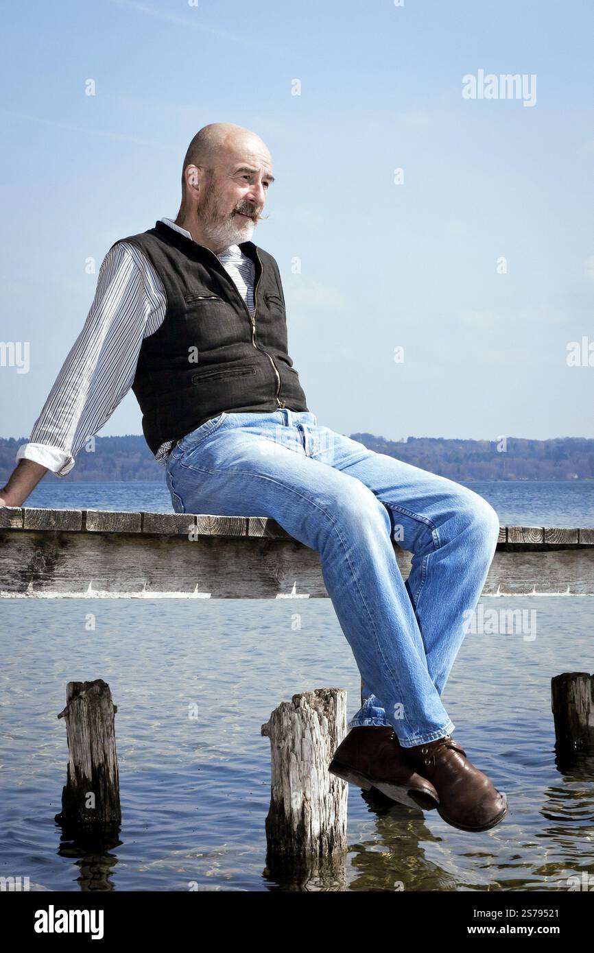 Ein alter Mann mit grauem Bart sitzt auf einem Steg Stockfoto