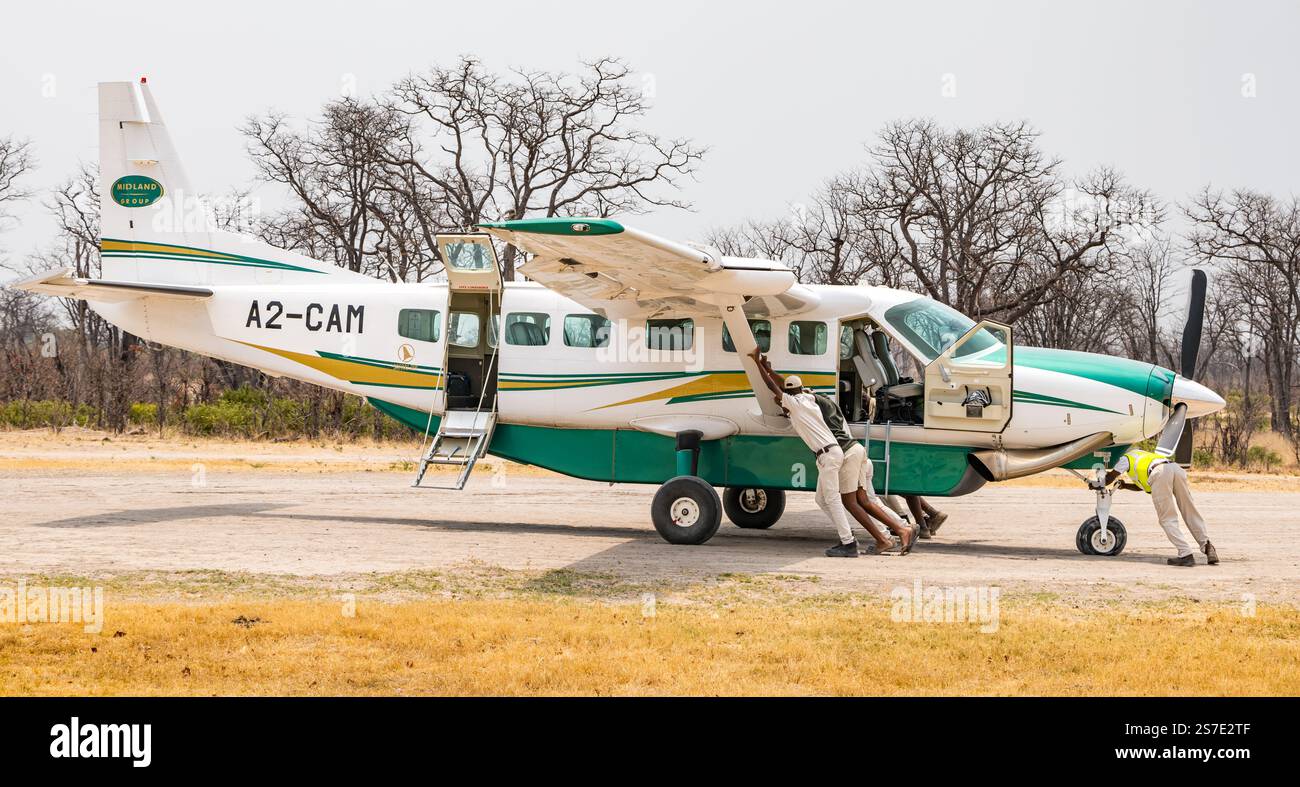 Safari-Guides schieben Touristenflugzeug mit Platten Reifen, Moremi Flugplatz, Botswana, Afrika Stockfoto