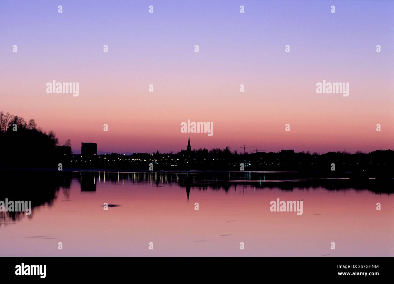 Skyline im Frühling. Farbenfroher Himmel, Gebäude am Fluss und Reflexionen im ruhigen Fluss. Kirche, Hotels und Lichter. Am späten Abend. Stockfoto