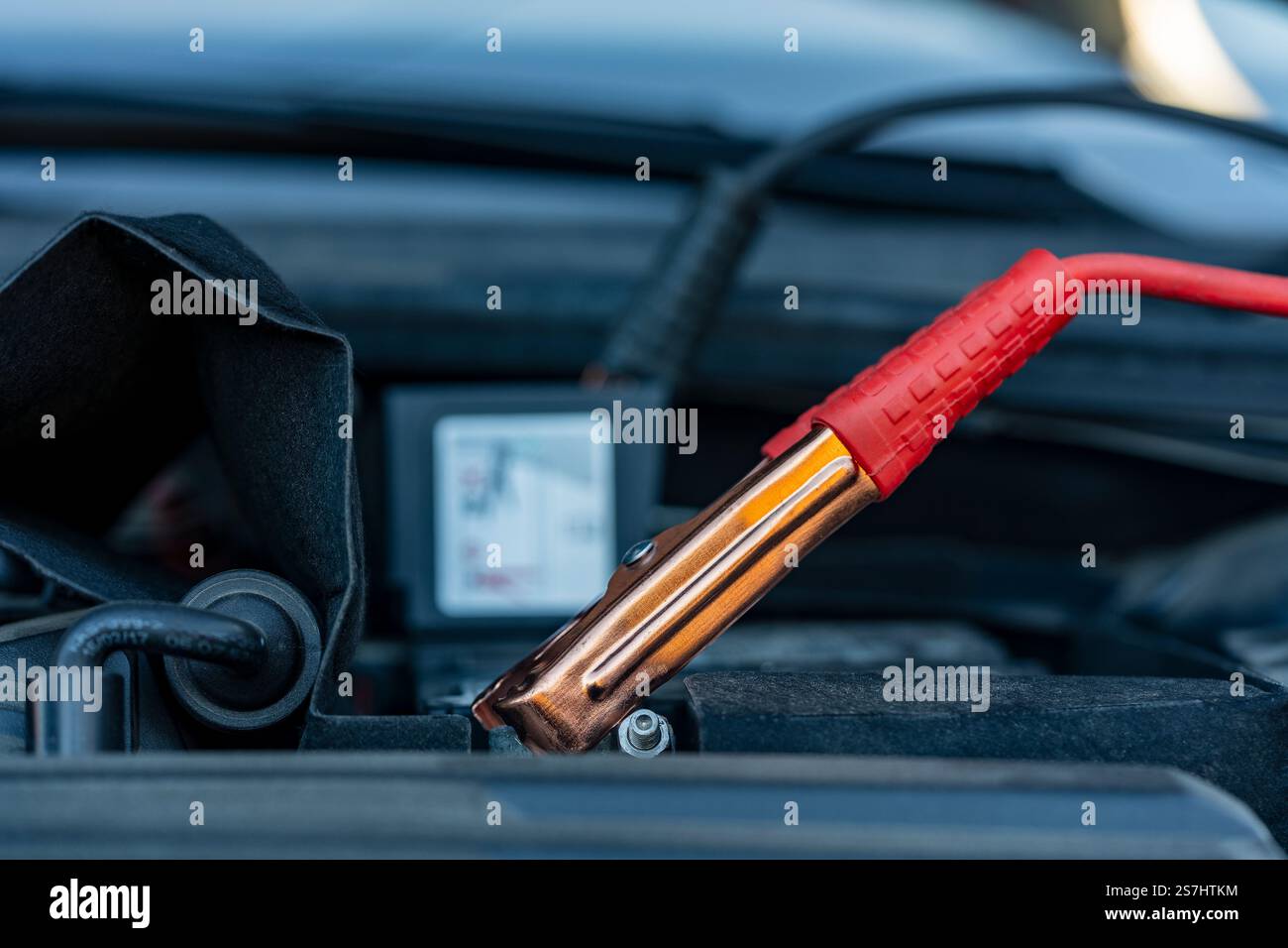 Autobatterie mit roten Überbrückungskabeln sicher befestigt, Nahaufnahme. Ladeklemme an Batterieklemme. Laden der alten Fahrzeugbatterie Stockfoto
