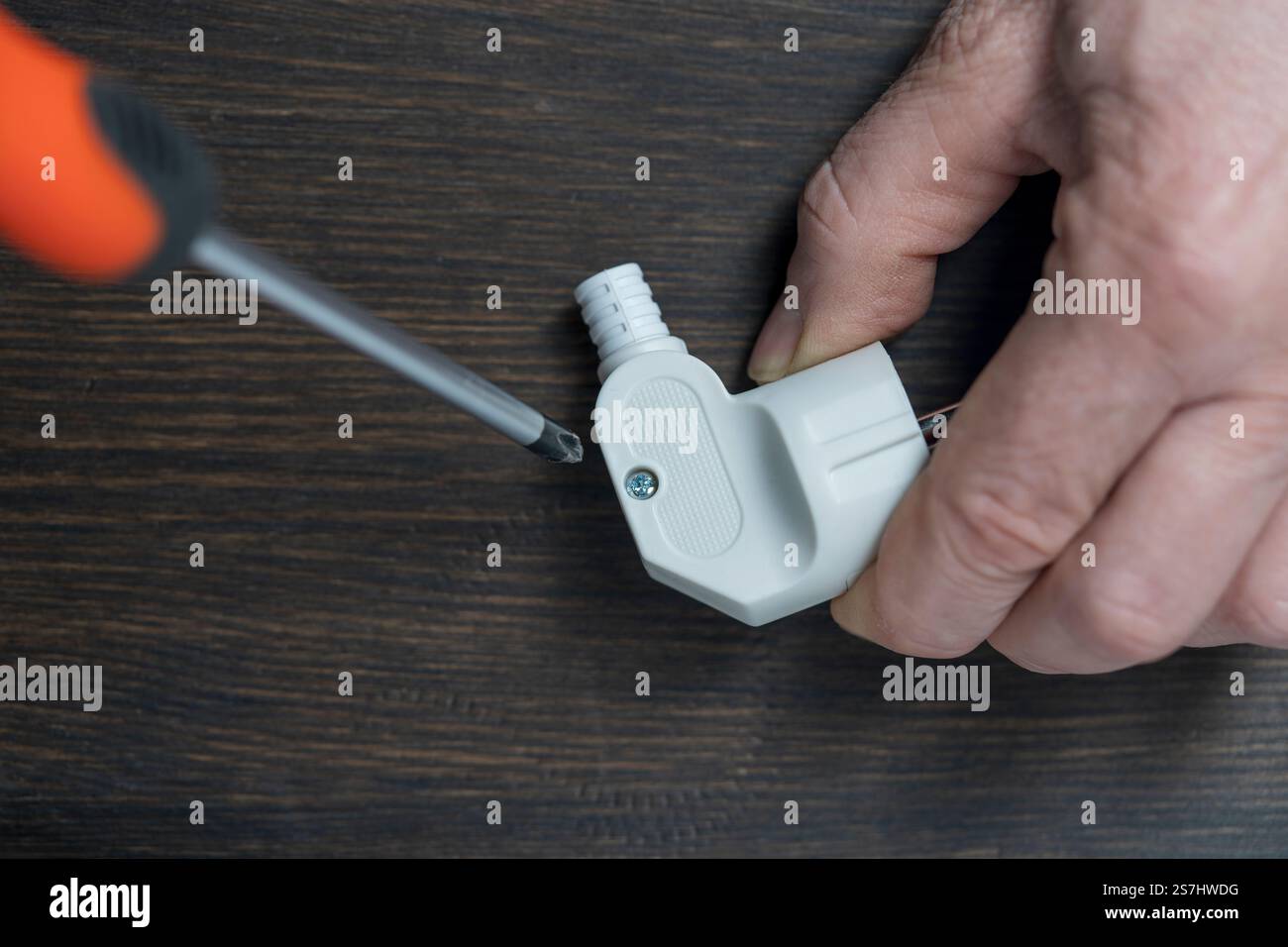 Lösen Sie mit einem Kreuzschlitzschraubendreher die Schraube am weißen Netzstecker, schließen Sie sie. Der Prozess der Analyse des Körpers der elektrischen plu aus Kunststoff Stockfoto