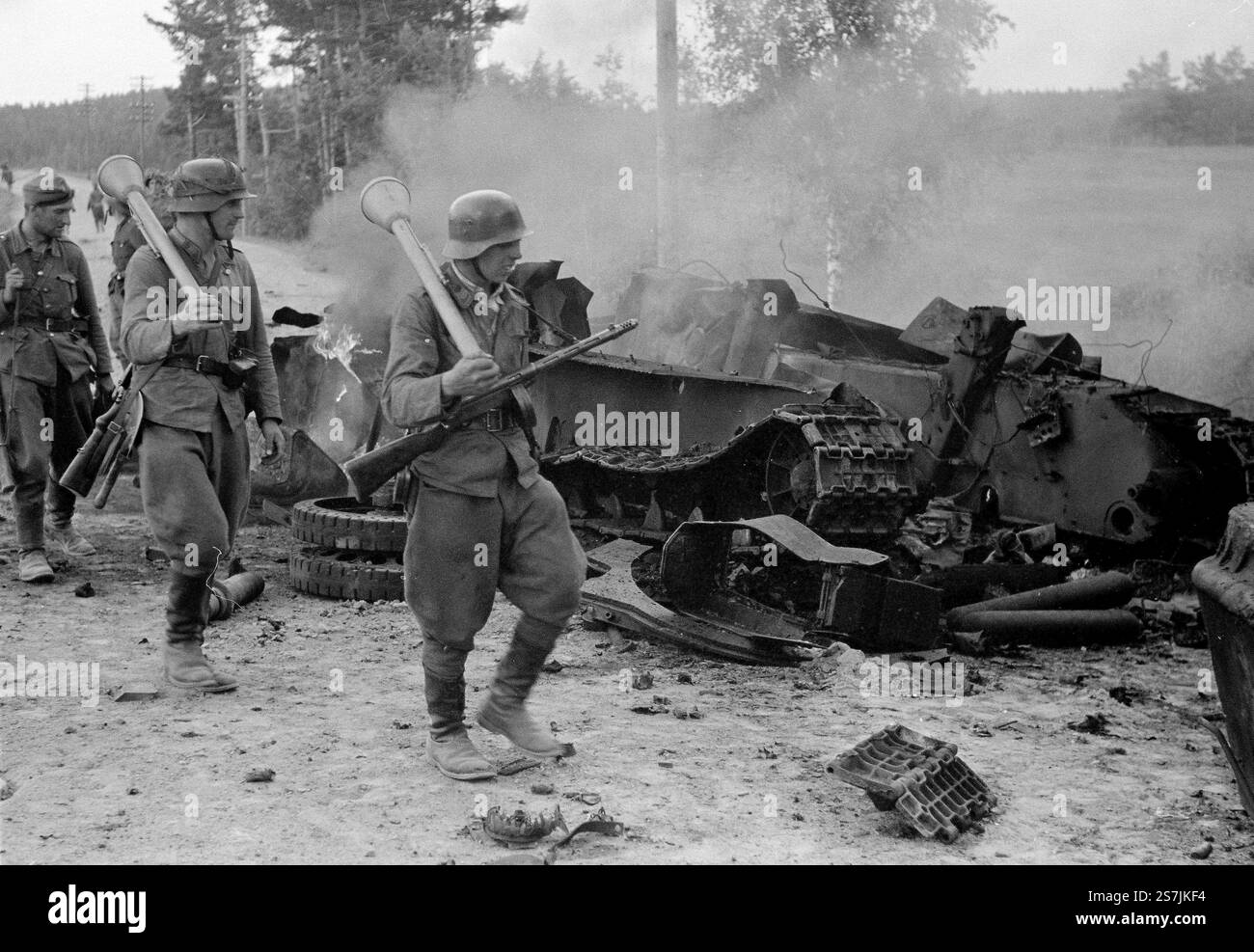 Finnische Soldaten, die Panzerfäuste auf ihren Schultern tragen, kommen an den Überresten eines zerstörten sowjetischen T-34-Panzers in der Schlacht von Tali-Ihantala im 2. Weltkrieg vorbei Stockfoto