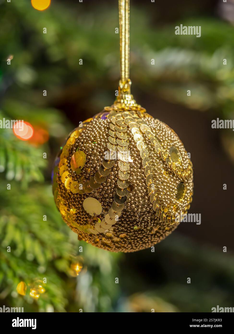 Eine festliche Dekoration mit goldenem Glitzerschmuck, hängt an einem Weihnachtsbaum, umgeben von sanften Lichtern und saisonalem Ambiente, EV Stockfoto