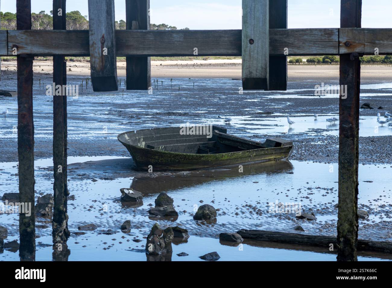 Das alte Boot ruht bei Ebbe an sonnigen Tagen im flachen Wasser unter dem hölzernen Pier Stockfoto