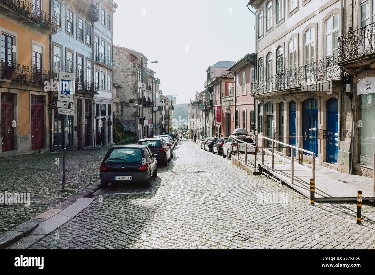 Eine malerische Kopfsteinpflasterstraße in Porto, Portugal, mit Autos auf beiden Seiten und historischen Gebäuden, die die Straße flankieren. Stockfoto