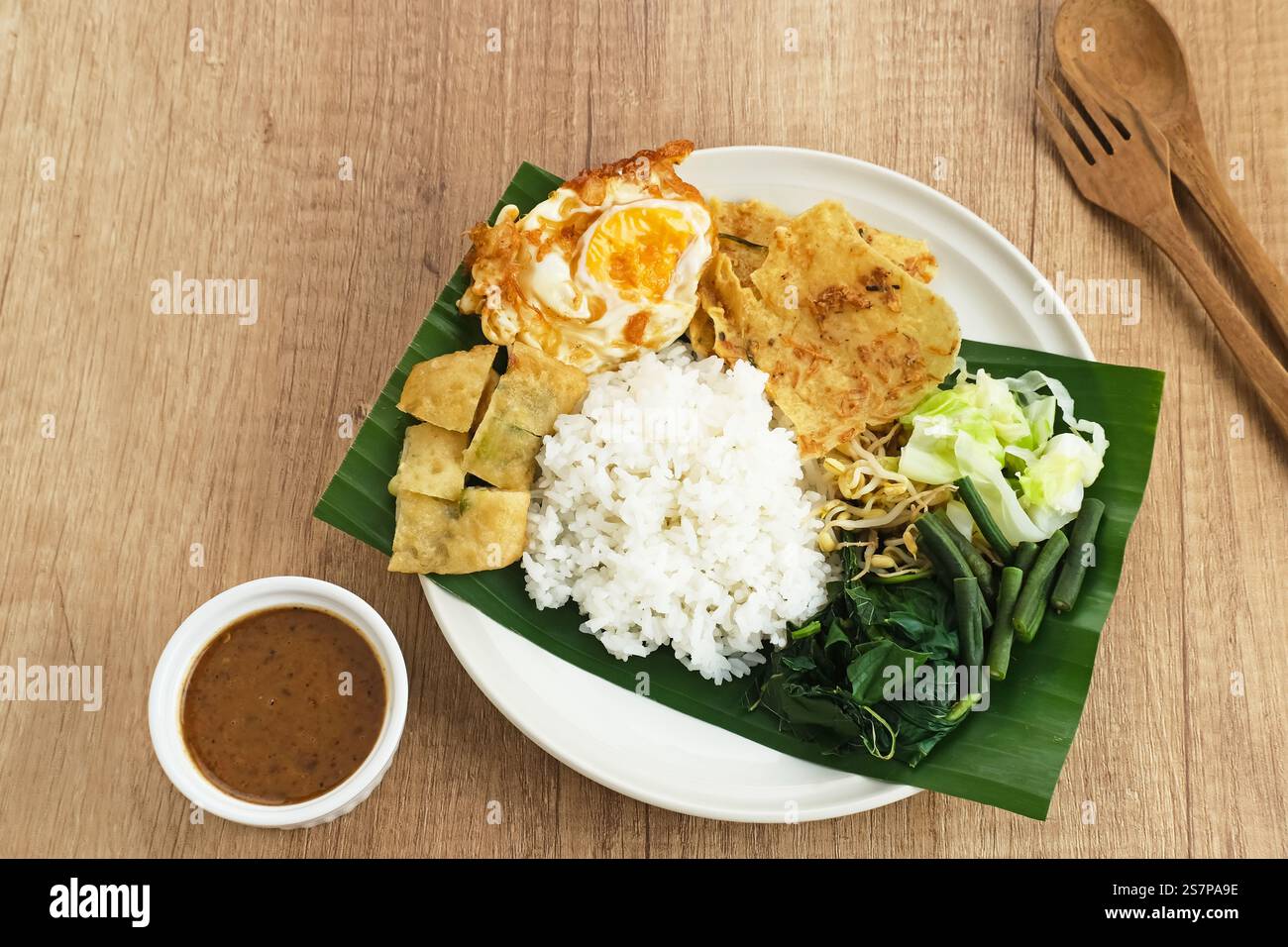 Nasi Pecel, ein traditioneller javanischer Reis mit Gemüsesalat und Erdnusssauce, serviert mit Beilagen wie Ei, Martinabak und Peyek Cracker. Stockfoto