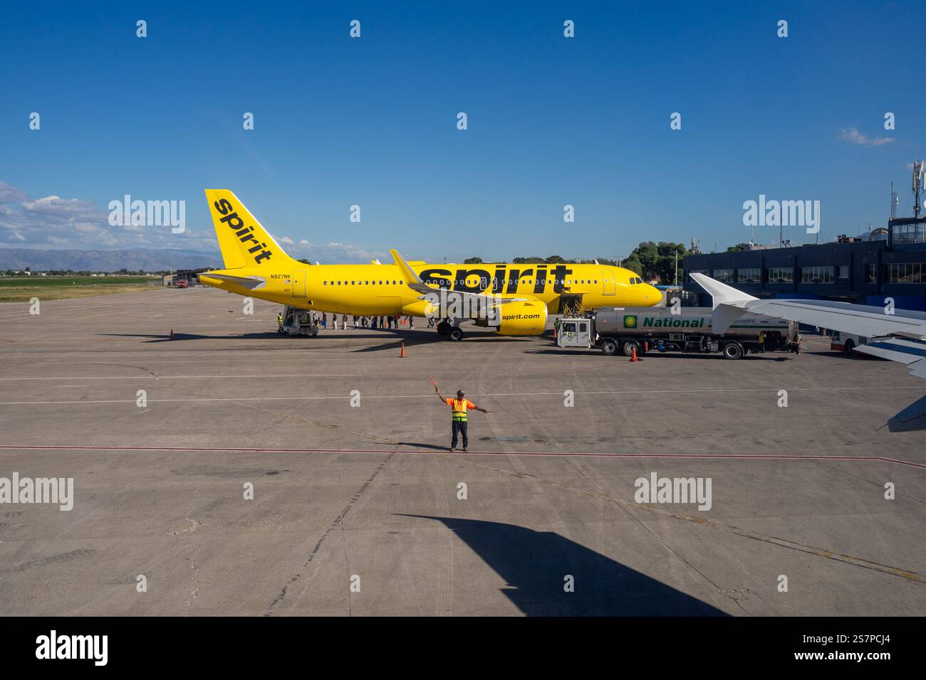 Weitwinkelansicht einer Asphaltfläche, auf der Spirit Airlines Passagiere aussteigen, während ein Luftmarshaller ein anderes Flugzeug aus dem Rahmen lenkt Stockfoto