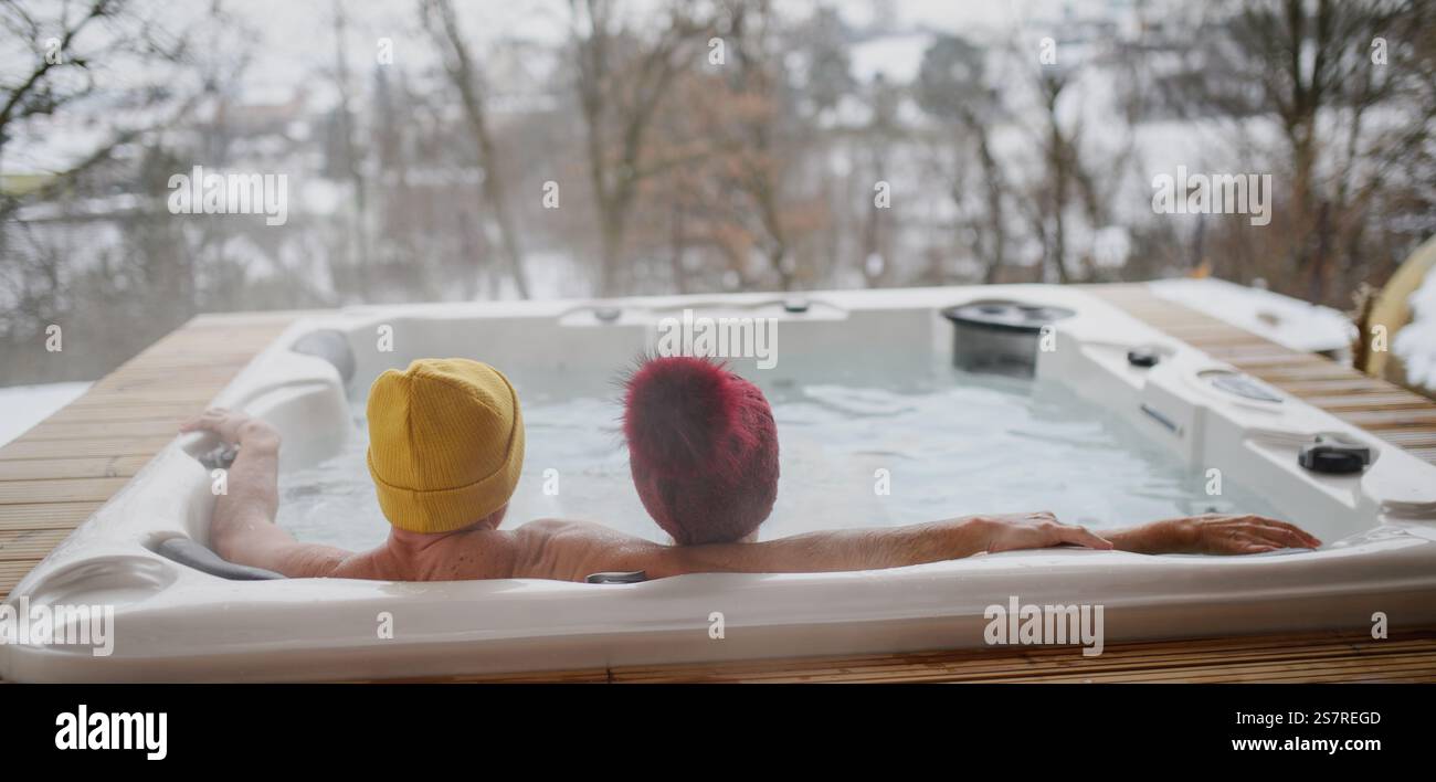 Rückansicht eines Seniorenpaares, das an kalten Wintertagen im Whirlpool badete. Banner mit Kopierbereich Stockfoto