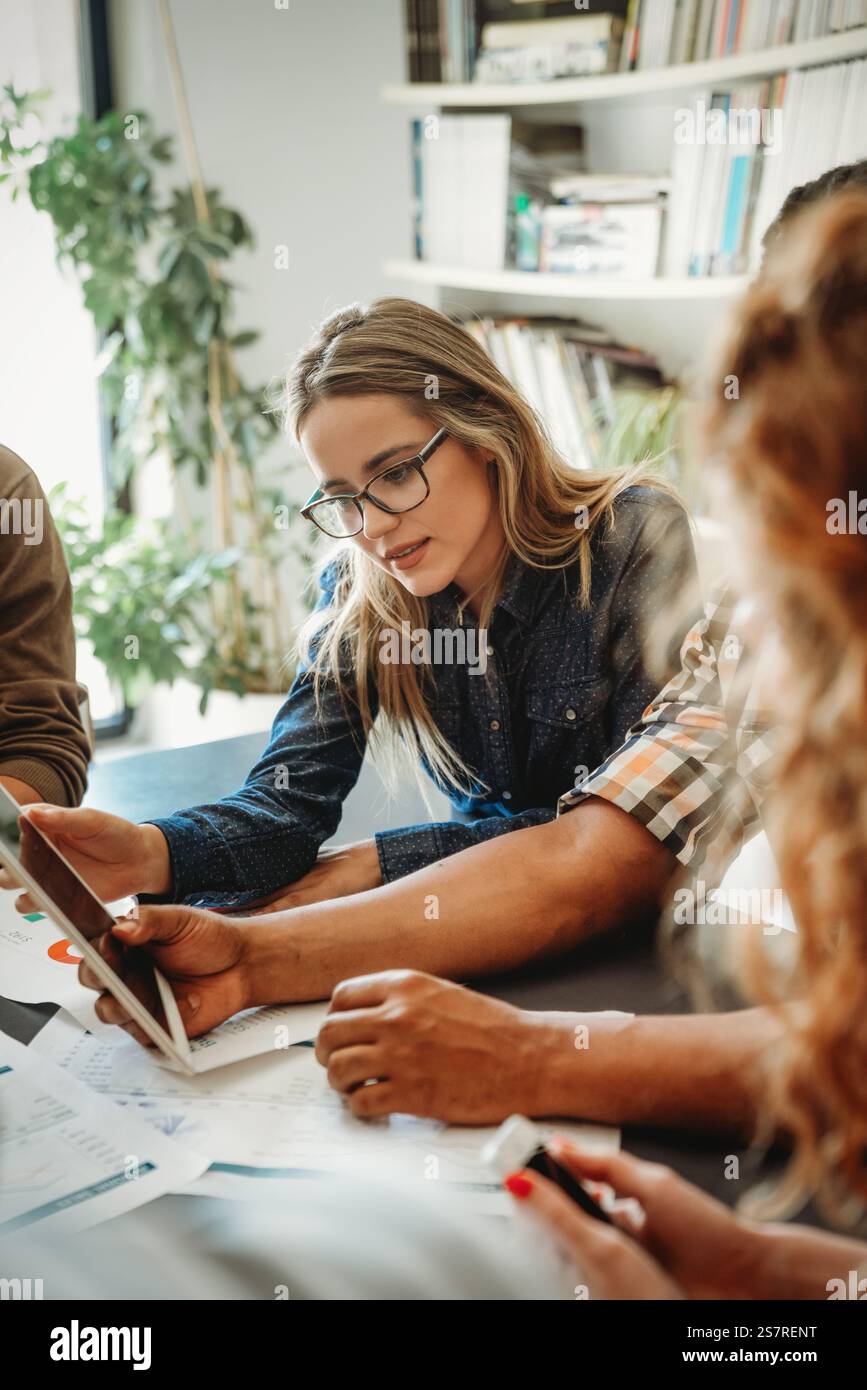 Lächelnd treffen sich verschiedene Kollegen in einem Brainstorming in der Vorstandsetage, um gemeinsam Finanzstatistiken zu diskutieren Stockfoto