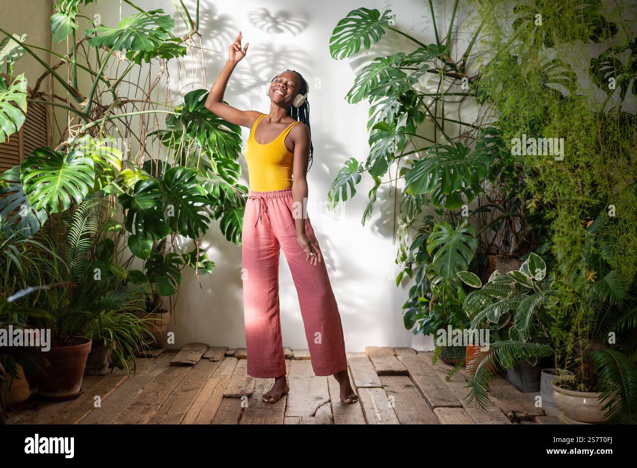 Unbeschwerte schwarze Frau tanzt barfuß, während Musik auf den Kopfhörern gehört wird. Stockfoto