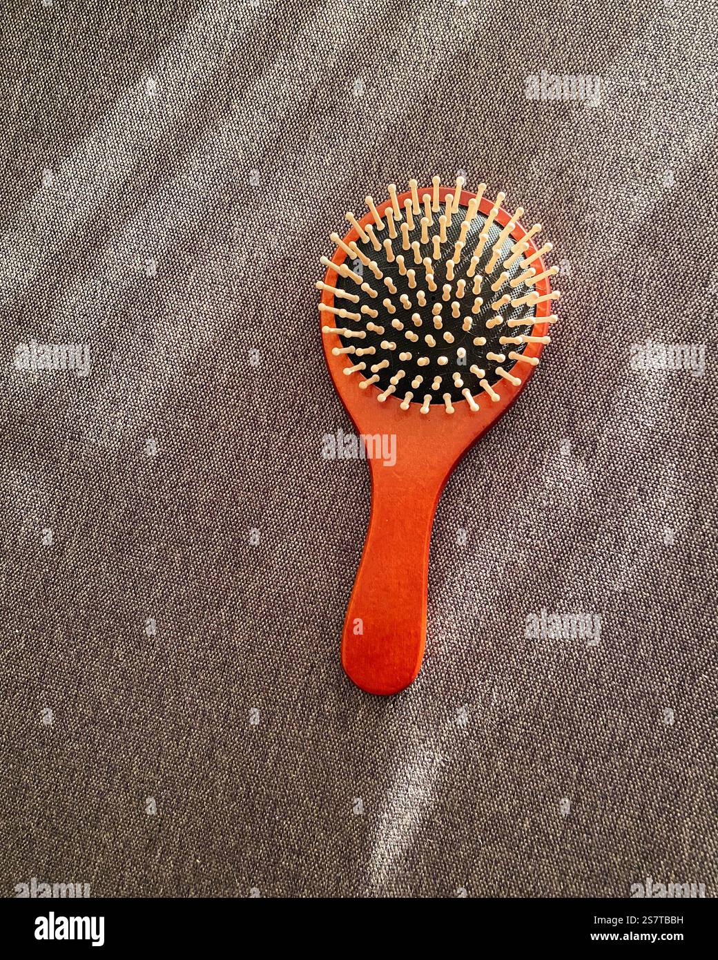 Orangefarbener Kamm auf braunem Tuch. Holzhaarkamm auf strukturierter Oberfläche mit Lichtstrahlen. Stockfoto