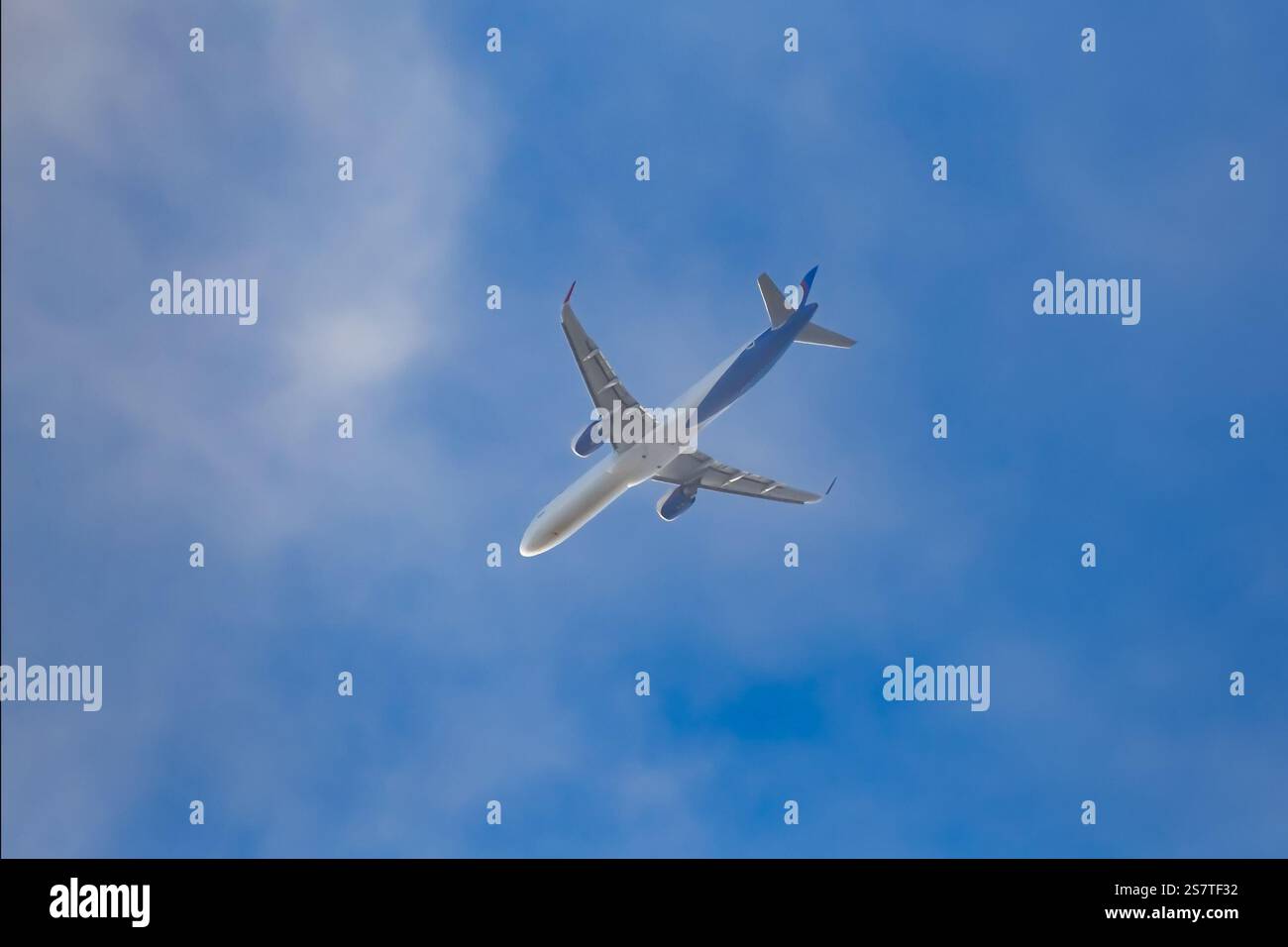 Passagierflugzeug, das vor blauem Himmel mit Wolken vorbeifliegt. Nahaufnahme, Ansicht von unten. Stockfoto